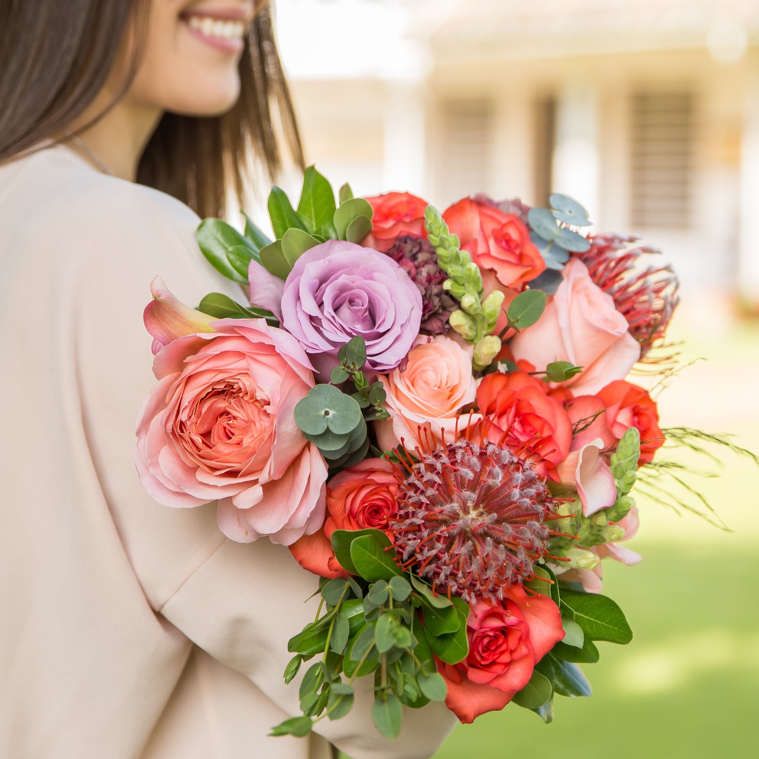 A woman holds a Designer Collection bouquet with Garden roses, snapdragons, pincushions, greenery, and other premium varieties.