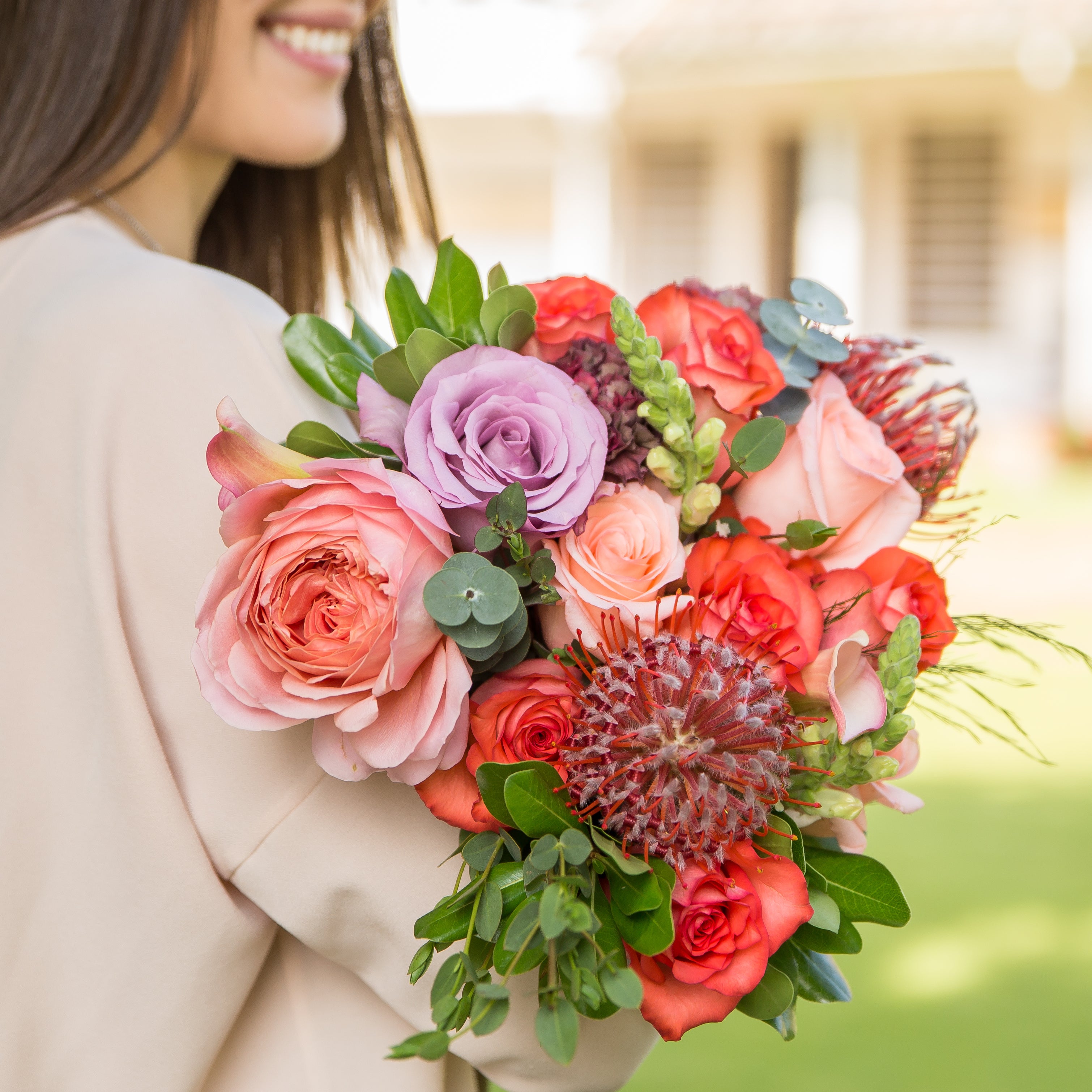 A woman holds a Designer Collection bouquet with Garden roses, snapdragons, pincushions, greenery, and other premium varieties.