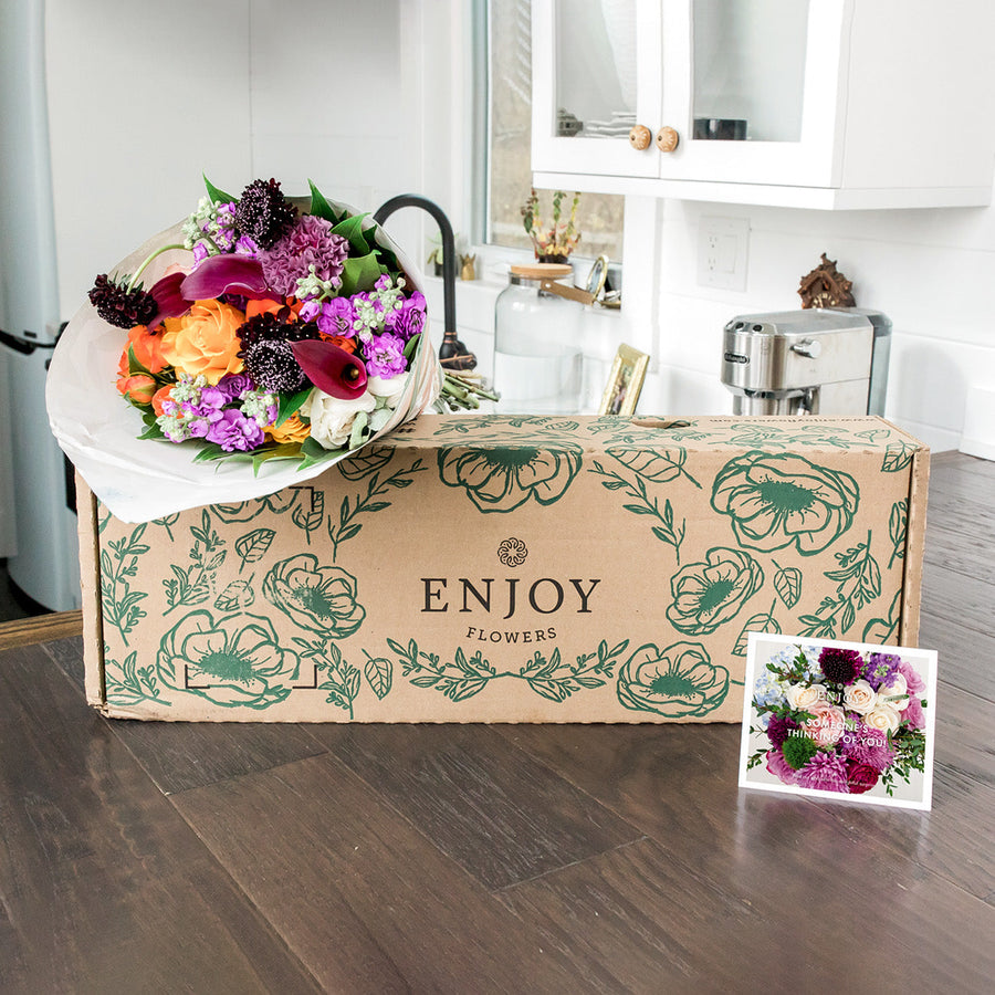 A Designer Collection delivery arrives with a box, card, and a fresh bouquet of 30-35 stems of Callas, scabiosa, roses, and other premium varieties. 